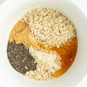 A white bowl containing oats, peanut butter, chia seeds, protein powder, and honey.