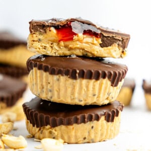 A stack of three chocolate peanut butter cups, with the top one bitten to reveal a peanut butter and jelly filling.