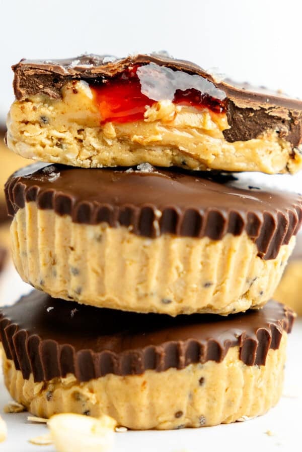 A stack of three chocolate peanut butter cups, with the top one bitten to reveal a peanut butter and jelly filling.