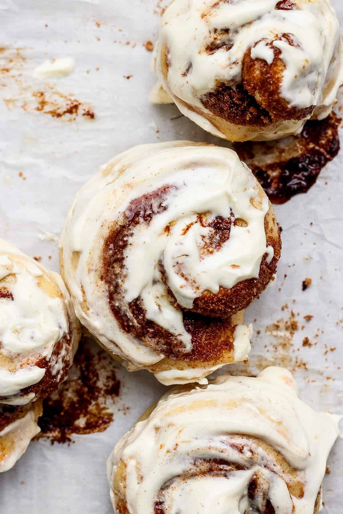 Top view of four cinnamon rolls with white icing on a parchment paper background.