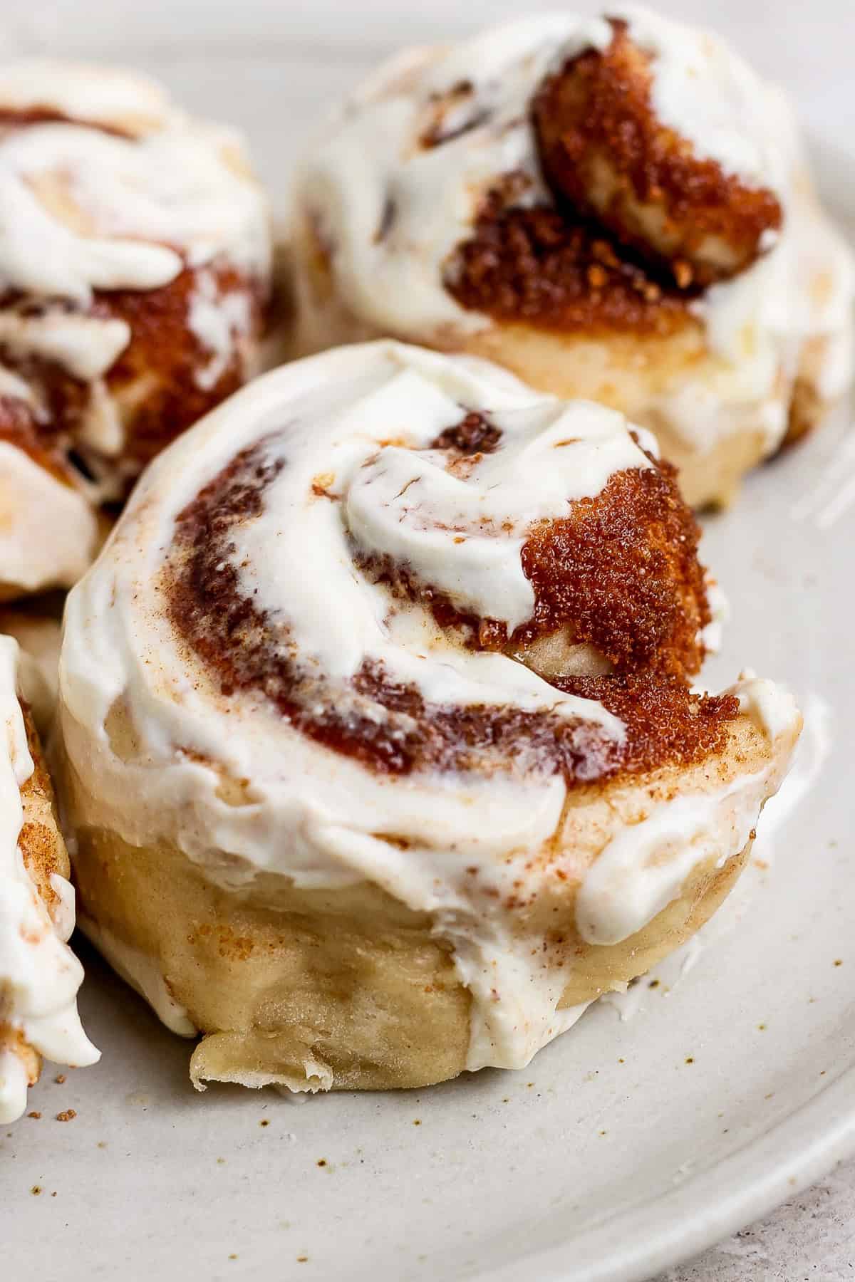 Close-up of freshly baked cinnamon rolls with creamy frosting on a white plate.