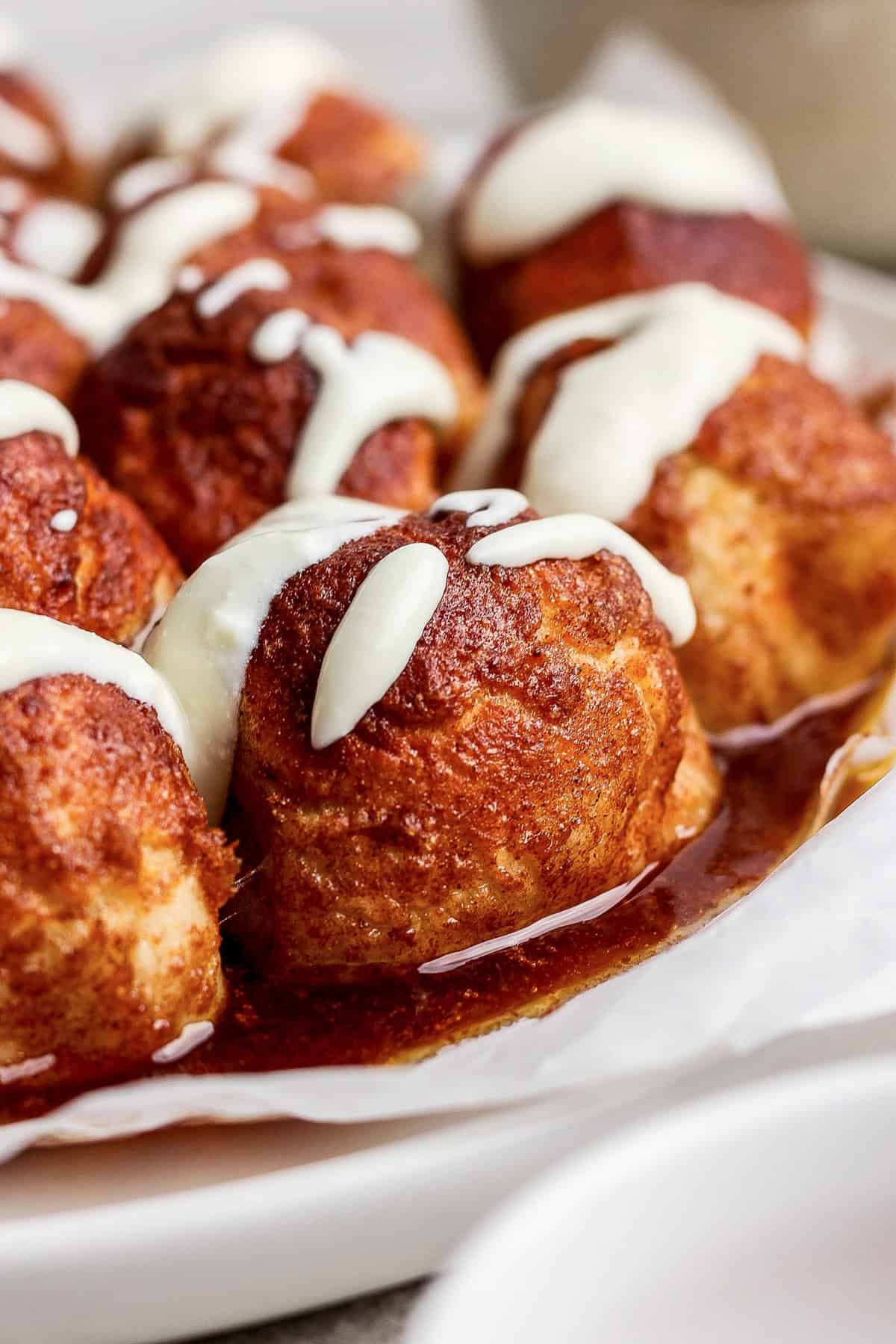 Close-up of cinnamon rolls topped with white icing, arranged on wax paper.