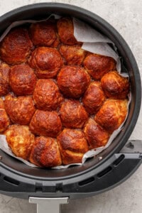 Golden brown bread rolls packed tightly in a round container with parchment paper.