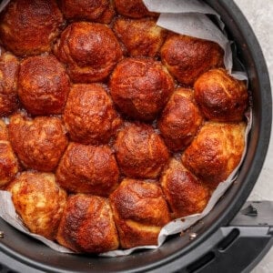 Golden brown bread rolls packed tightly in a round container with parchment paper.