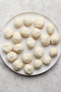 A white plate with 20 evenly spaced raw dough balls on a textured surface.