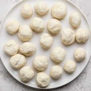 A white plate with 20 evenly spaced raw dough balls on a textured surface.