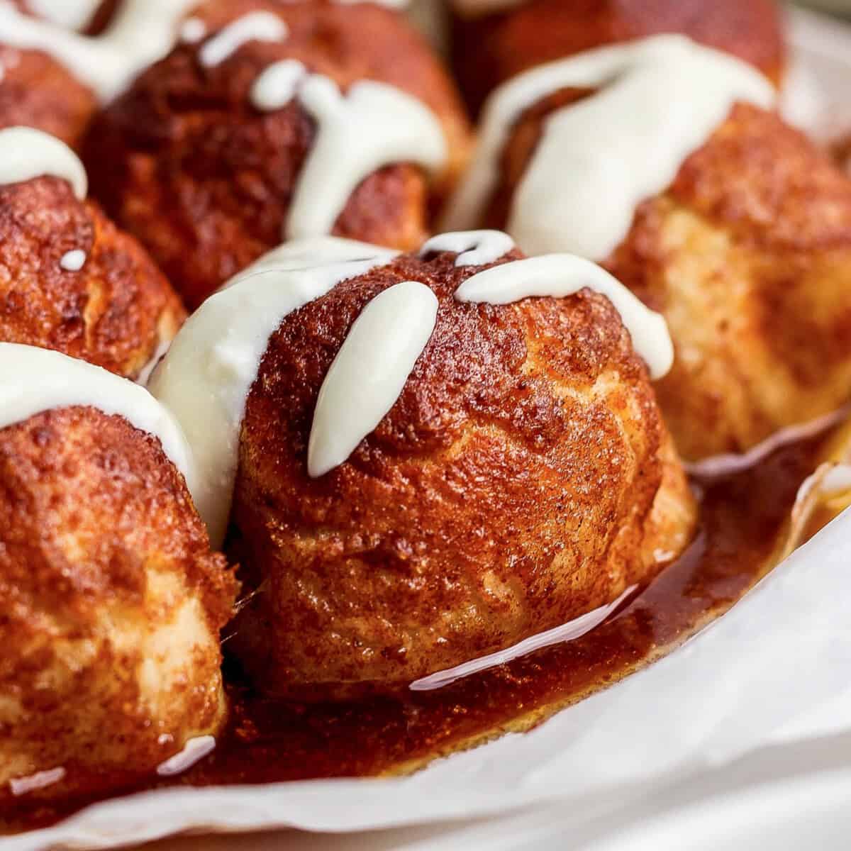 Close-up of cinnamon rolls topped with white icing and glazed with syrup.