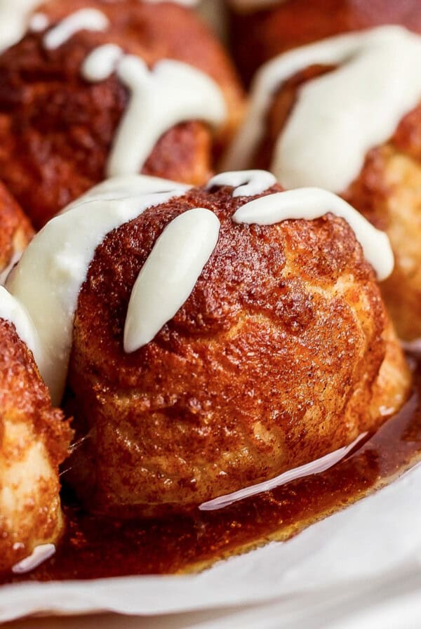 Close-up of cinnamon rolls topped with white icing and glazed with syrup.