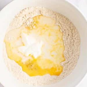 A white bowl containing flour with a well in the center holding cracked eggs and yogurt.