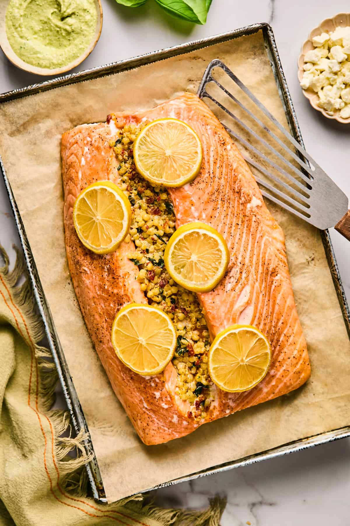 Baked salmon fillet stuffed with couscous and topped with lemon slices on a parchment-lined baking tray, with a spatula beside it.