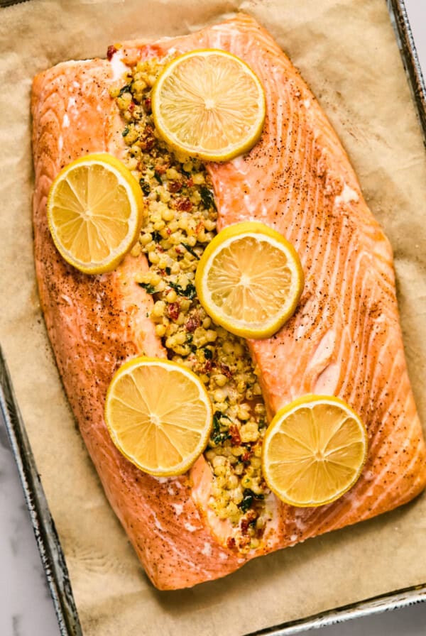 Baked salmon fillet stuffed with a mixture, topped with lemon slices on parchment paper in a baking tray.