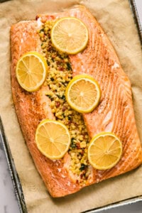 Baked salmon fillet stuffed with couscous and topped with lemon slices on a parchment-lined baking sheet.