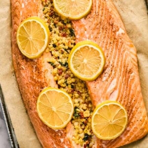 Baked salmon fillet stuffed with couscous and topped with lemon slices on a parchment-lined baking sheet.