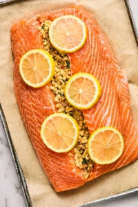 Raw salmon fillet stuffed with seasoned breadcrumbs and topped with lemon slices on parchment paper.