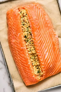 Salmon fillet on parchment paper, split open and filled with a mixture of couscous, herbs, and spices.