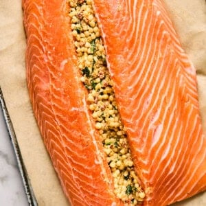 Salmon fillet on parchment paper, split open and filled with a mixture of couscous, herbs, and spices.