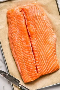 A raw salmon fillet on parchment paper with a knife beside it.