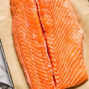 A raw salmon fillet on parchment paper with a knife beside it.