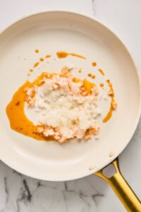 Chopped onions and oil in a white frying pan on a marble countertop.