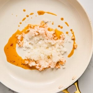 Chopped onions and oil in a white frying pan on a marble countertop.