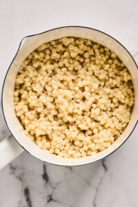 A pot filled with cooked pearl couscous on a marble surface.