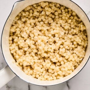 A pot filled with cooked pearl couscous on a marble surface.