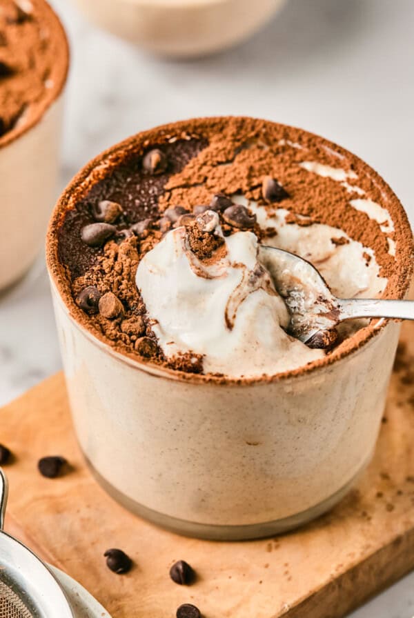 Tiramisu in a ceramic cup topped with cocoa powder and chocolate chips, with a spoon scooping a portion.
