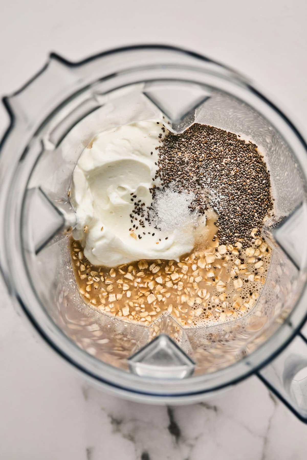 Ingredients in a blender: yogurt, chia seeds, salt, oats, and a liquid.