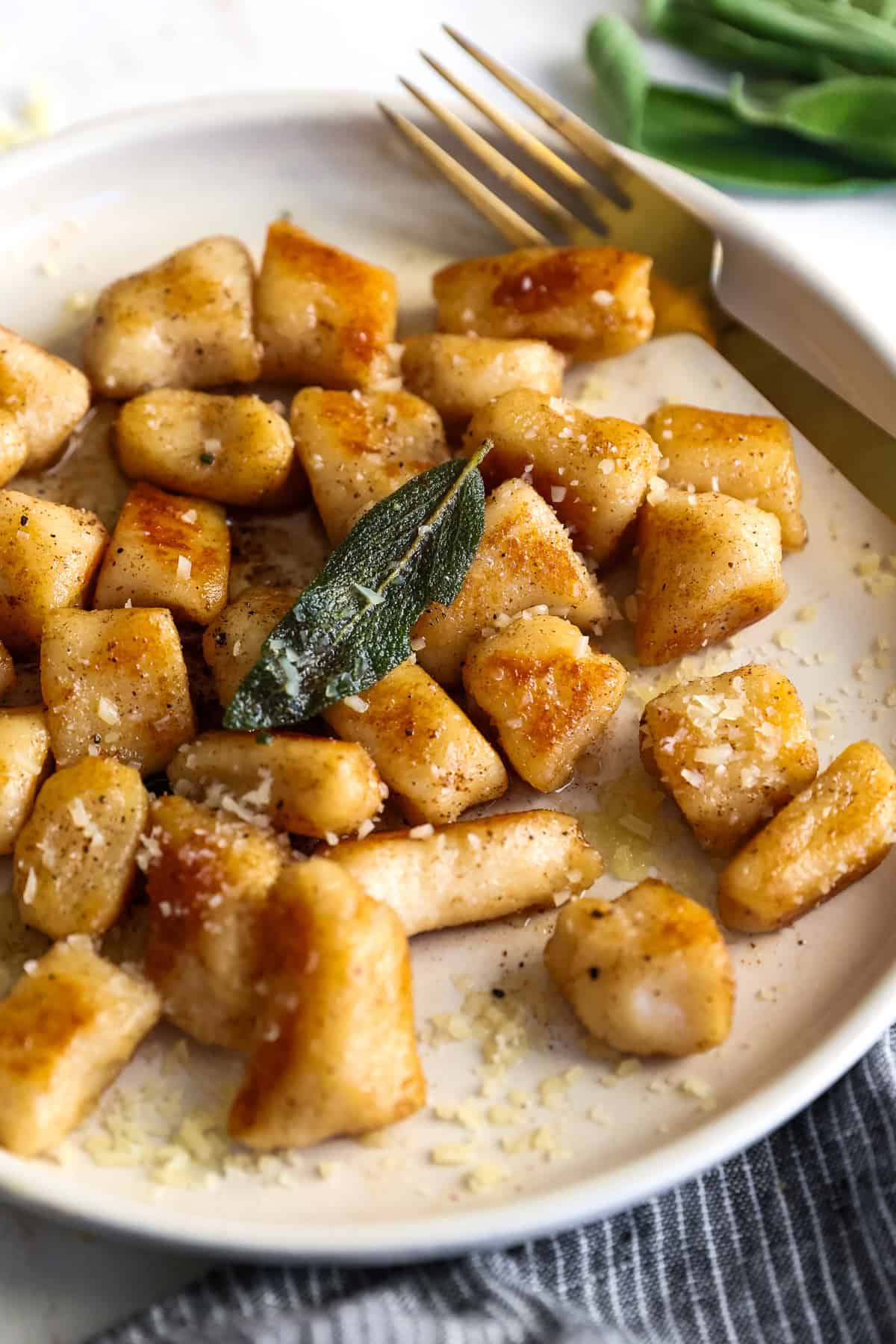 A plate of cottage cheese gnocchi topped with grated cheese and garnished with a sage leaf. A fork rests on the plate beside the gnocchi.