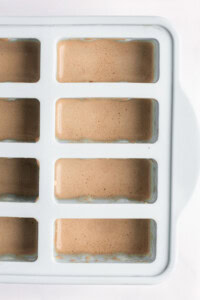 Ice tray filled with light brown liquid, viewed from the top.