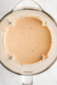 A top view of a blender containing a smooth, light brown liquid mixture.