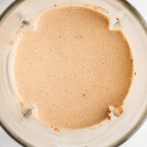 A top view of a blender containing a smooth, light brown liquid mixture.