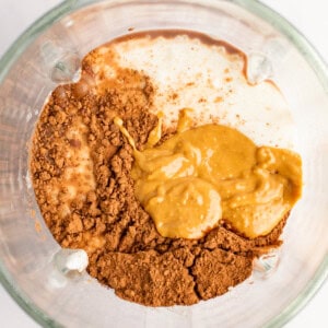 Top view of a blender jar containing cocoa powder, peanut butter, and milk, ready to be blended.