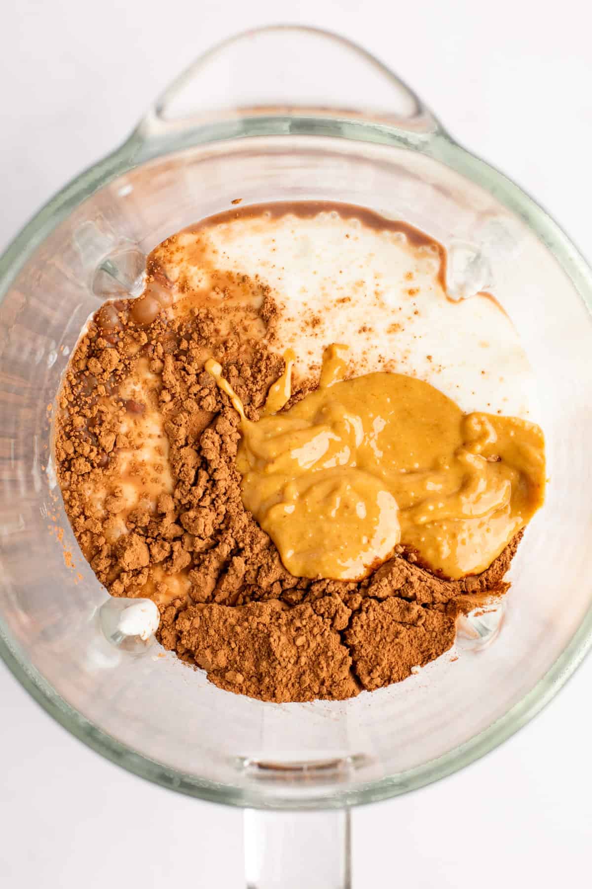 Top view of a blender jar containing cocoa powder, peanut butter, and milk, ready to be blended.