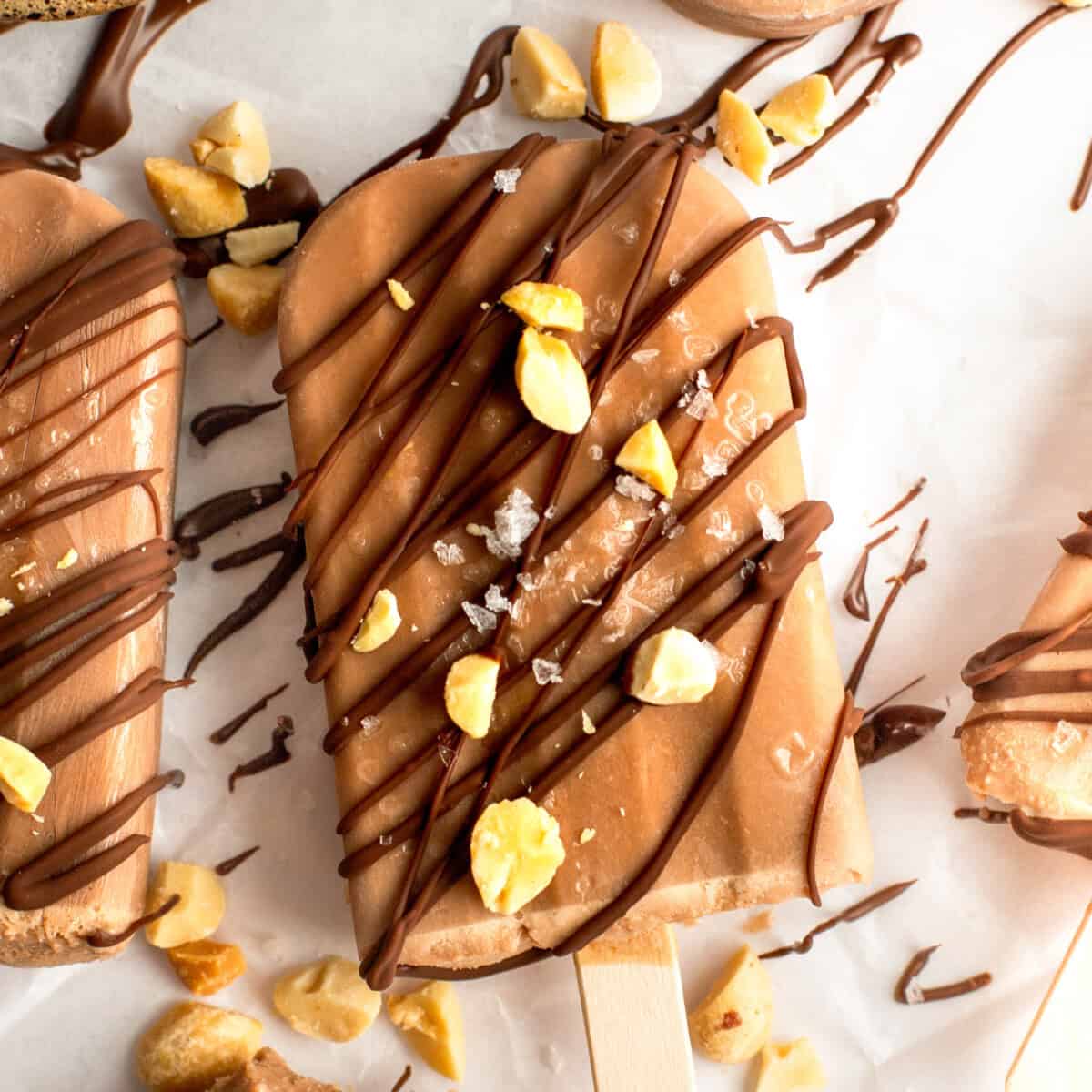 Chocolate-coated ice cream bar sprinkled with nuts and drizzled chocolate on parchment paper.