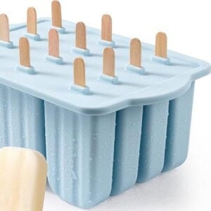 Blue popsicle mold with twelve wooden sticks inserted, shown alongside a single cream-colored protein fudgesicle in the foreground.