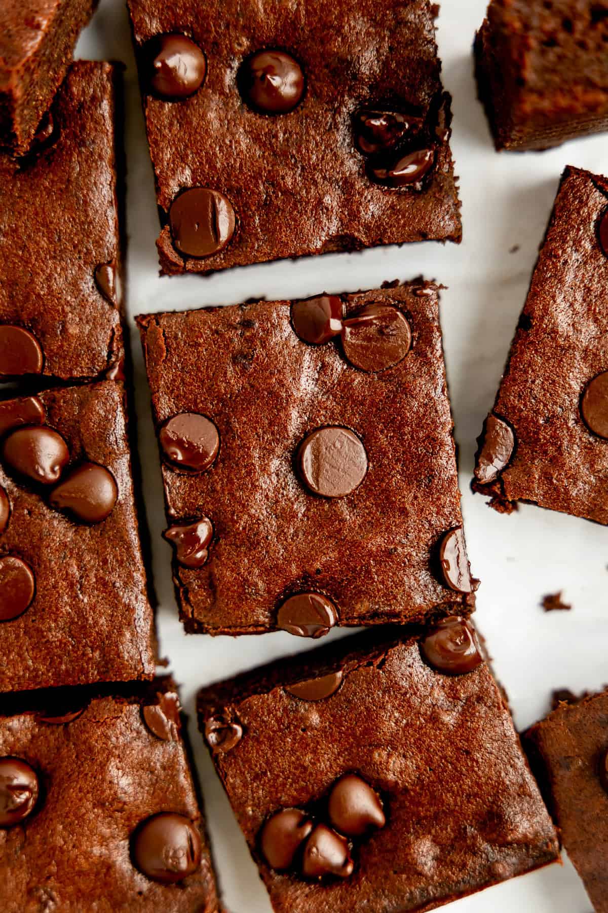 Close-up of sliced chocolate brownies topped with chocolate chips on a white surface.