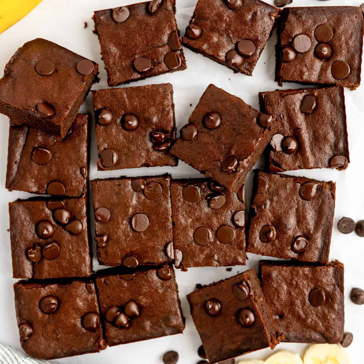 Sliced chocolate brownies with chocolate chips on top, arranged on a white surface.