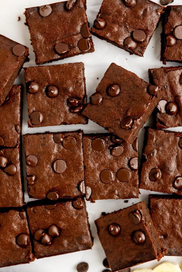 Sliced chocolate brownies with chocolate chips on top, arranged on a white surface.