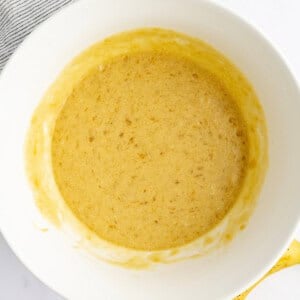 Bowl of mashed banana mixture, with a partially visible ripe banana and striped cloth nearby.