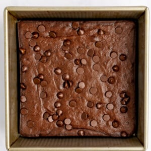 A square baking pan filled with chocolate brownie batter topped with chocolate chips, ready for baking.