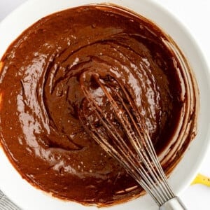 Bowl of chocolate batter with a whisk, surrounded by scattered chocolate chips and a banana.