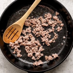 Ground beef cooking in a black cast iron skillet with a wooden spatula resting inside.