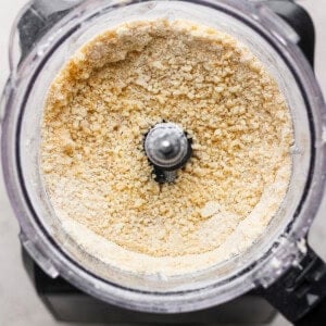 Top view of a food processor on a counter containing crushed graham crackers with a metal blade in the center.