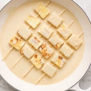 Skewered tofu cubes in creamy marinade on a round white dish.