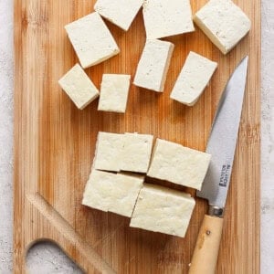 Cubed tofu on a wooden cutting board with a knife.