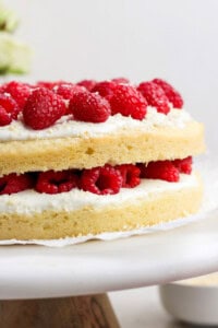 Layered cake with white frosting and fresh raspberries on a cake stand.