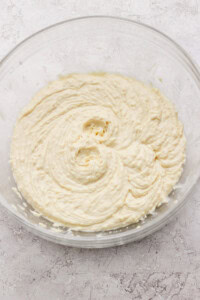 A glass bowl filled with creamy, light yellow cake batter on a textured white surface.