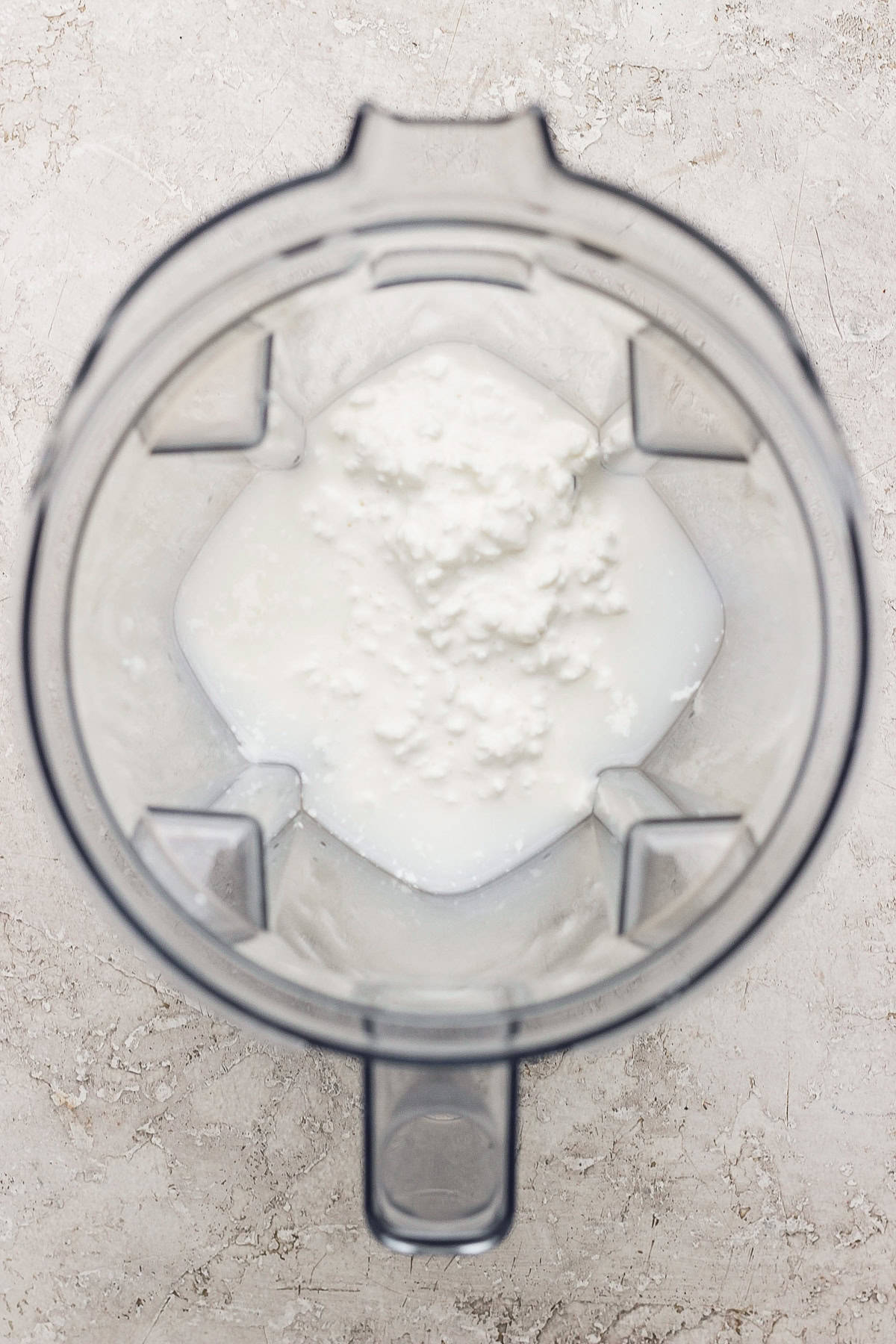 Blender jug with foamy white liquid inside, viewed from above.