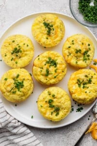 Seven egg muffins topped with chopped chives on a white plate.